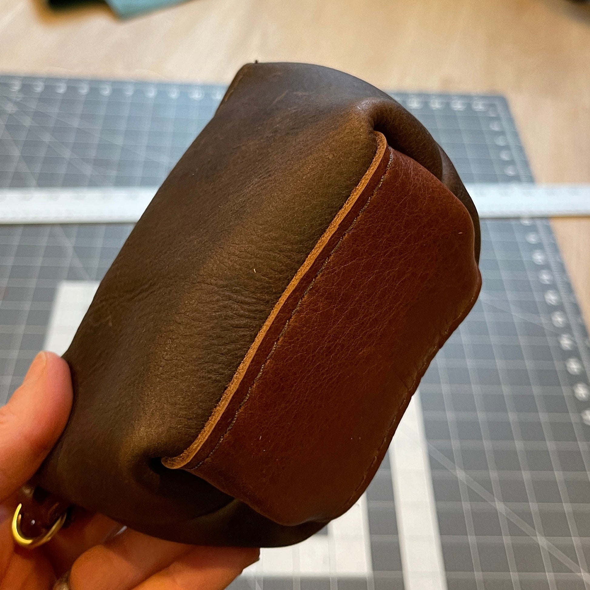 Brown leather pouch held in a hand on a grid surface with a blurred background