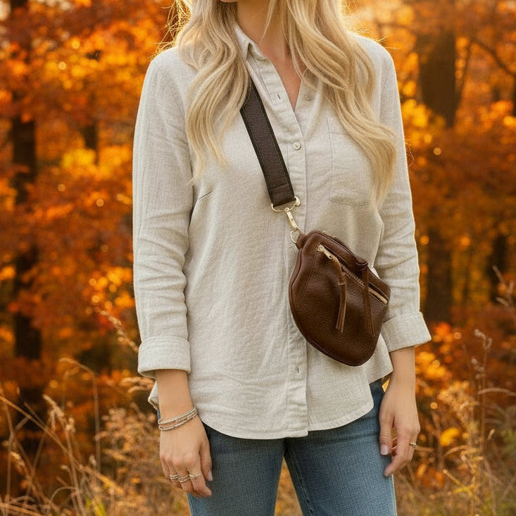 Woman standing in a field with a sunset in the background wearing handmade leather bag.