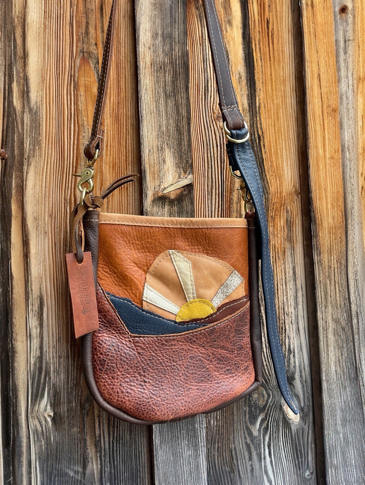 Brown leather crossbody bag with decorative elements on a wooden background