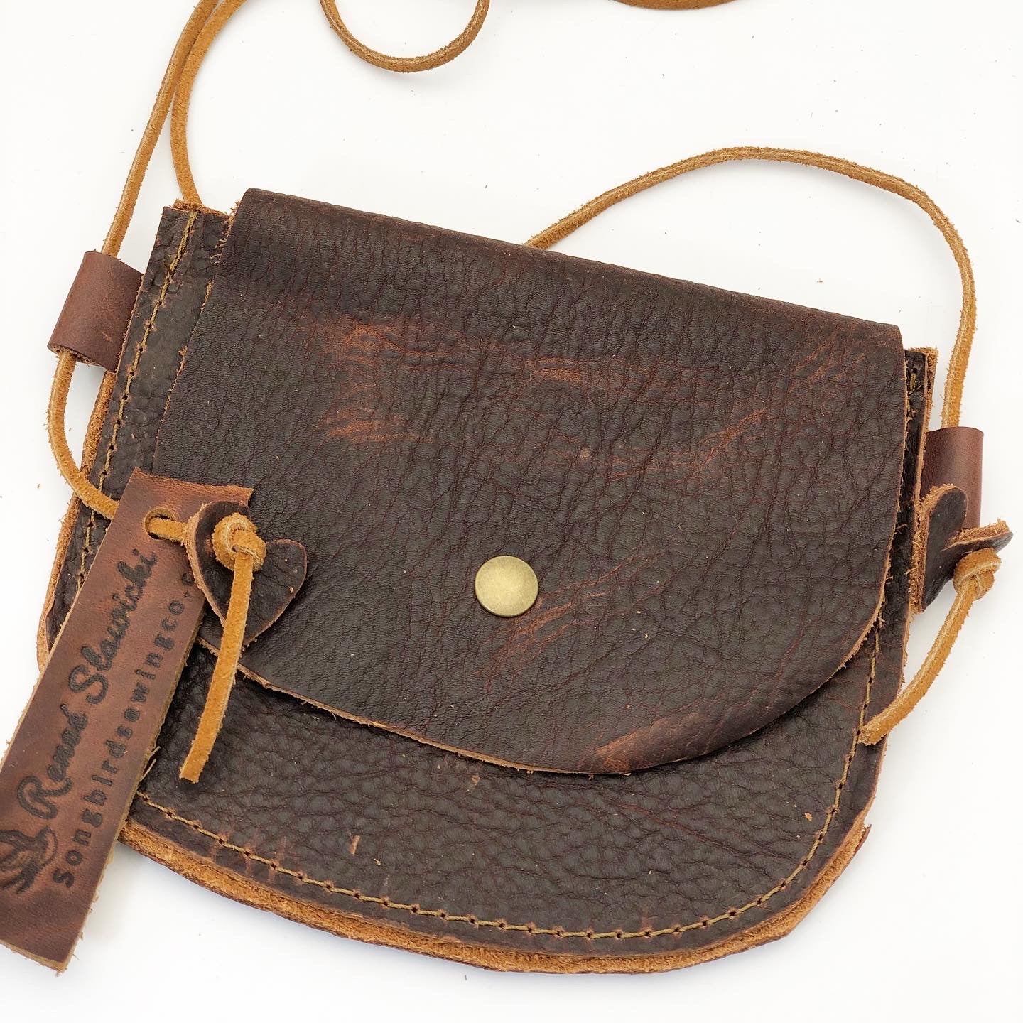 A brown leather purse with a raw hide string, knot, and brass snap closure.